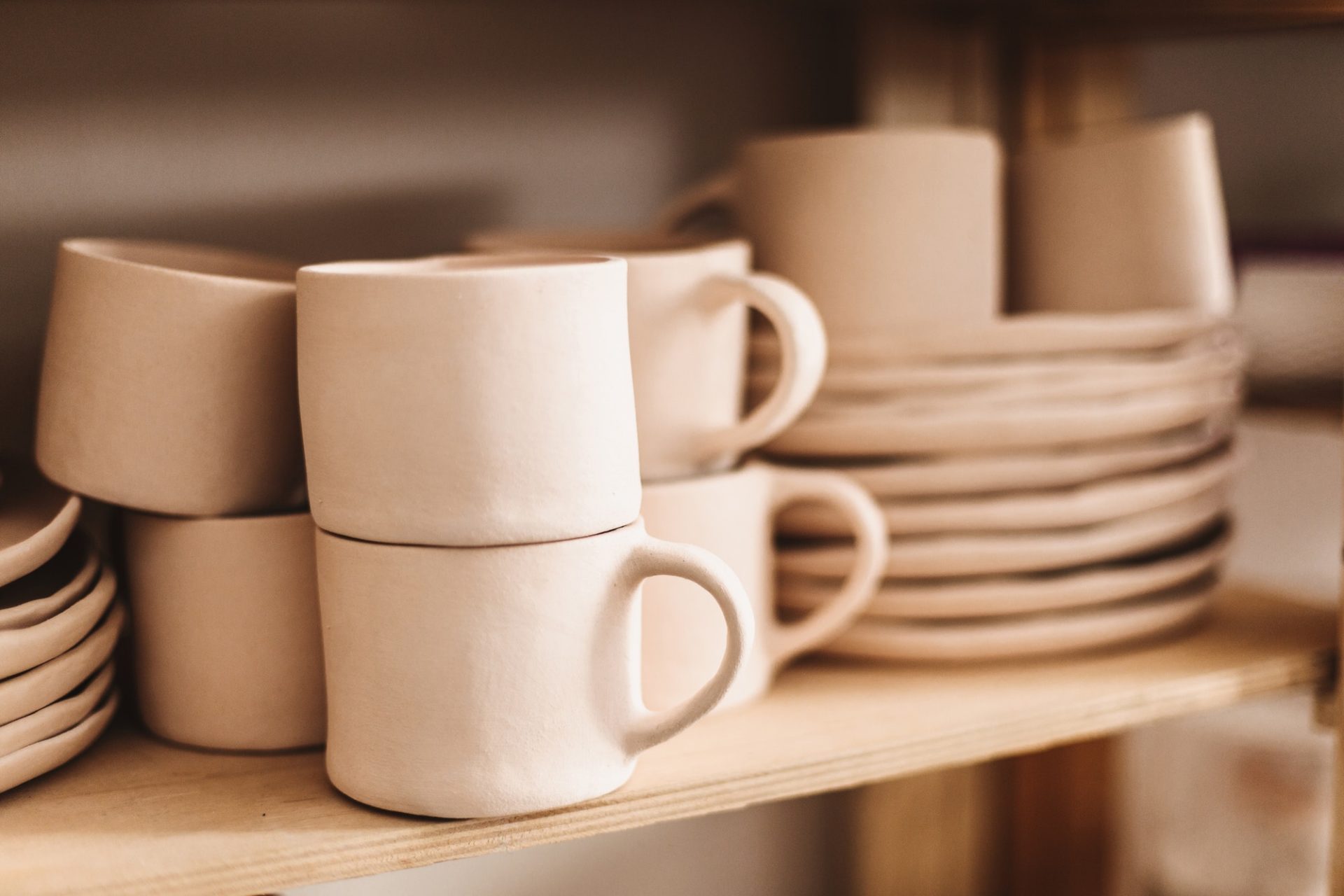 Close up handmade clay mugs and cups on wooden shelves at pottery studio