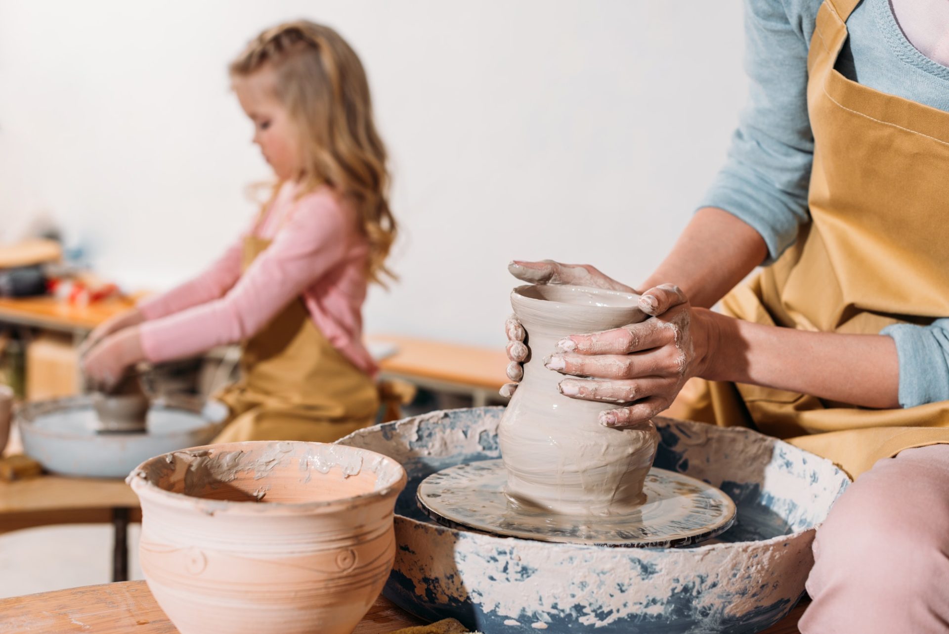 selective focus of daughter making ceramic pot on pottery wheel with mother on foreground