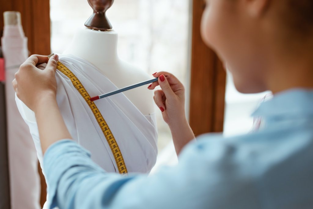 Young designer with tape is measuring white dress. Designers studio