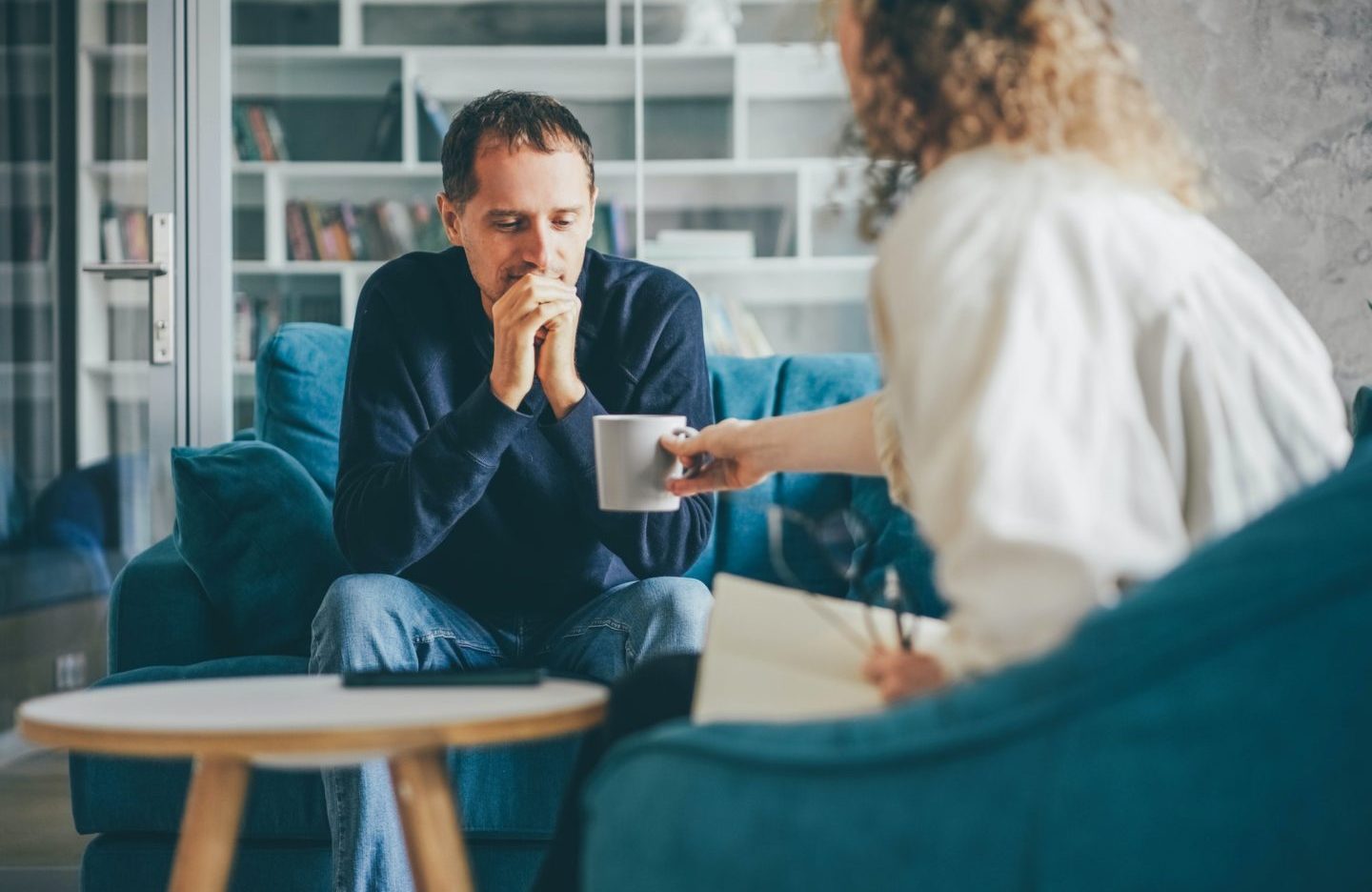 Curly haired woman consultant offers cup of coffee to stressed man client