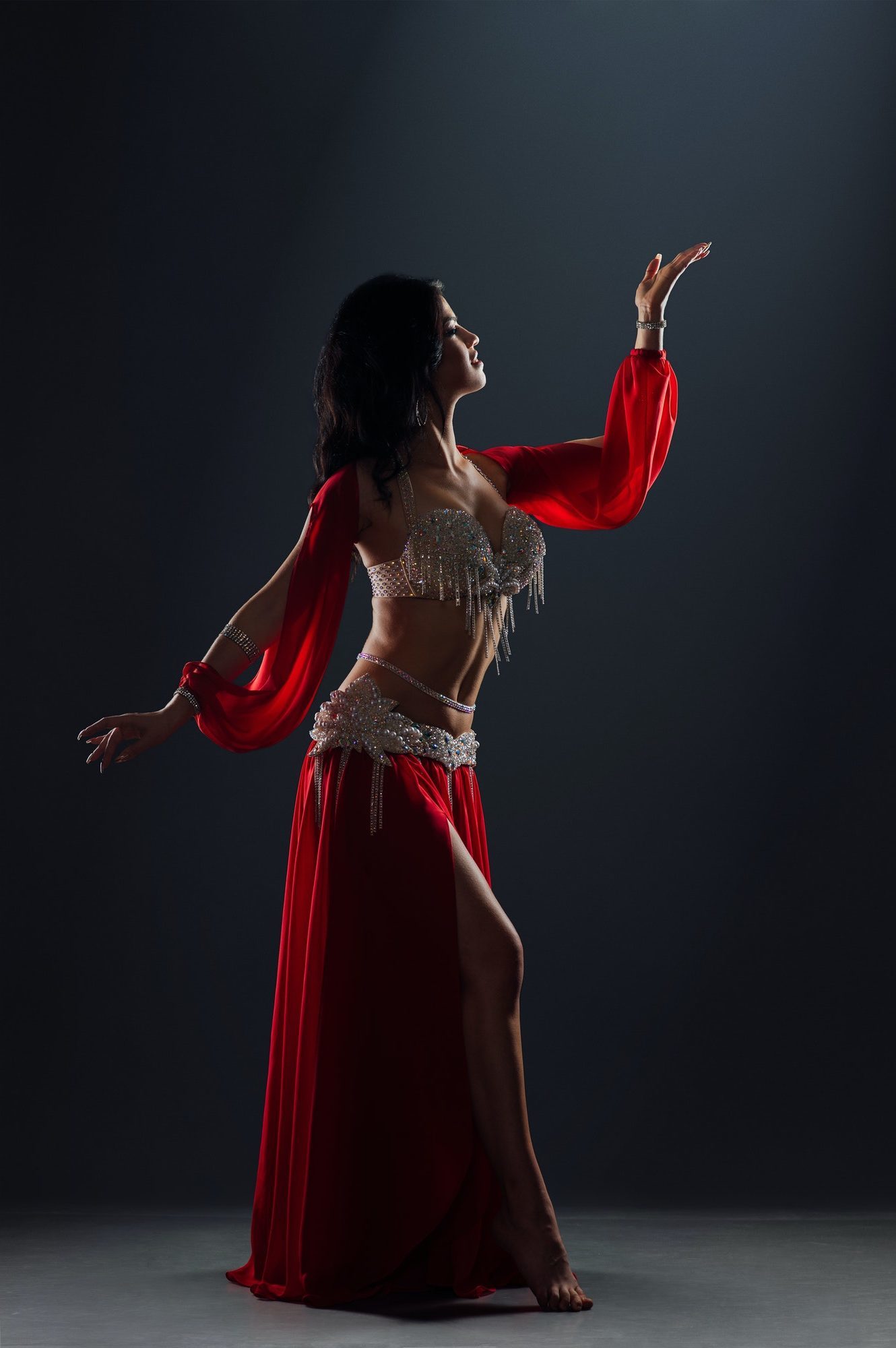 beautiful black-haired girl in red ethnic dress dancing oriental dances on stage in the dark
