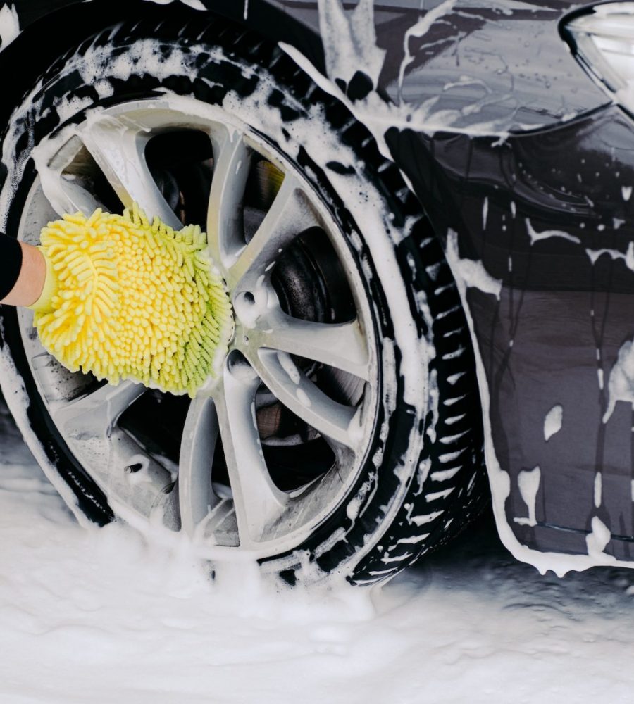 Workers hand with yellow sponge washing car wheels with detergent for cleaning vehicles