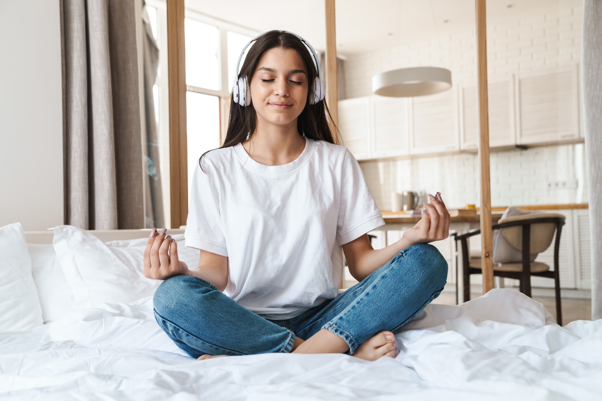Photo of smiling woman using wireless headphone while meditating
