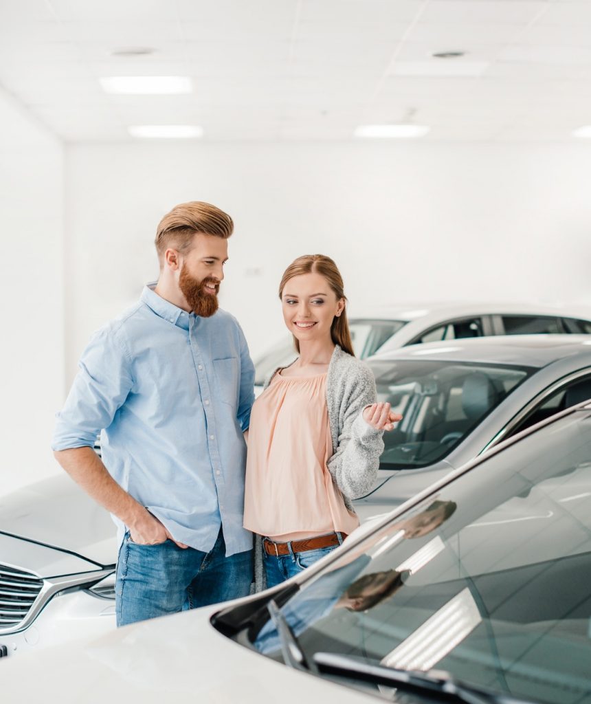 Happy couple choosing car in dealership salon, woman pointing on car