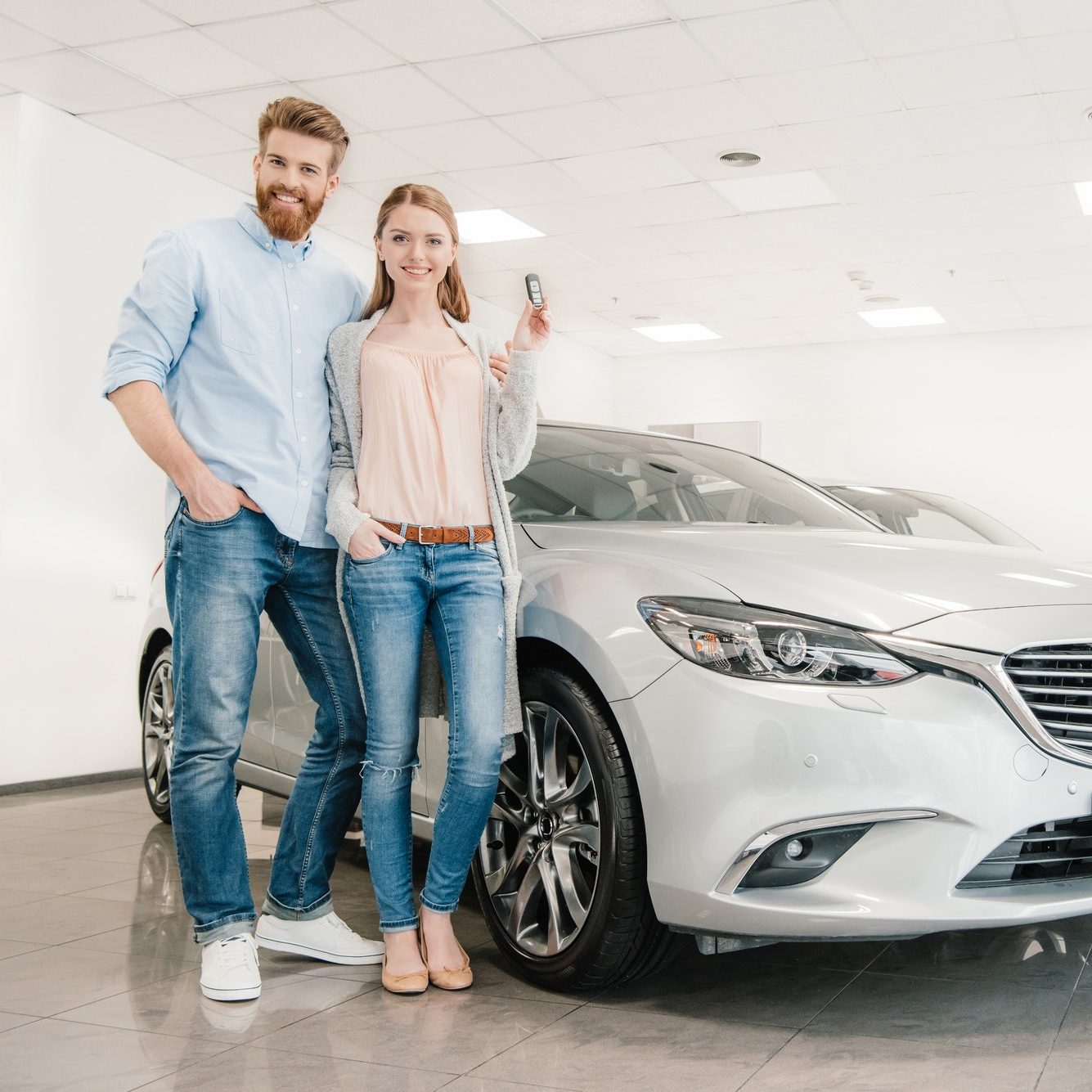 Happy couple with car key standing at car in dealership salon