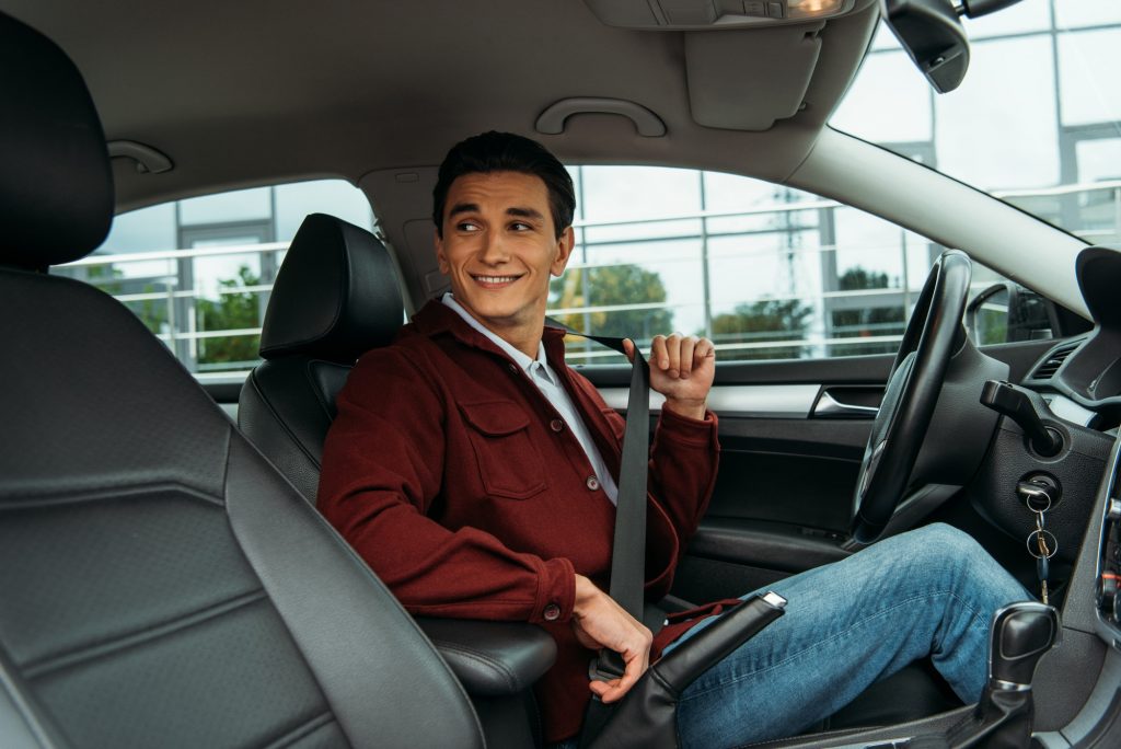 Smiling man holding safety belt in car and looking away