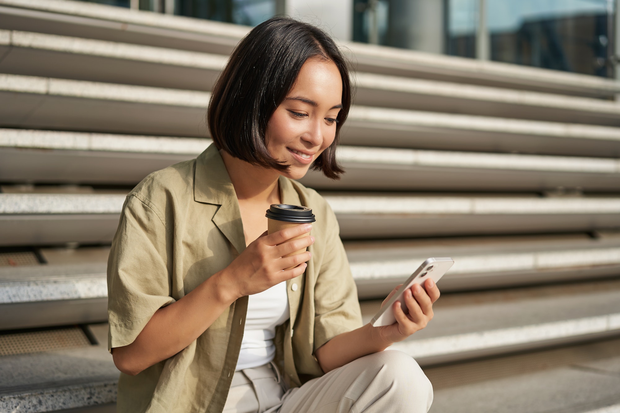 Portrait of asian woman with smartphone, drinks coffee and watches videos on mobile phone. Girl