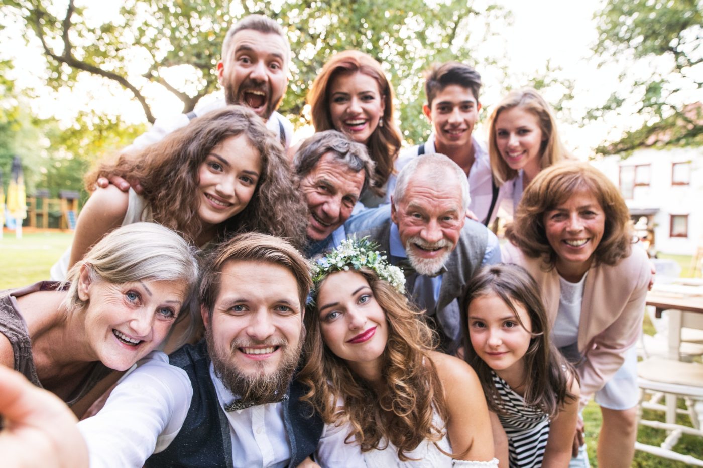 Bride, groom with guests taking selfie at wedding reception outside in the backyard.