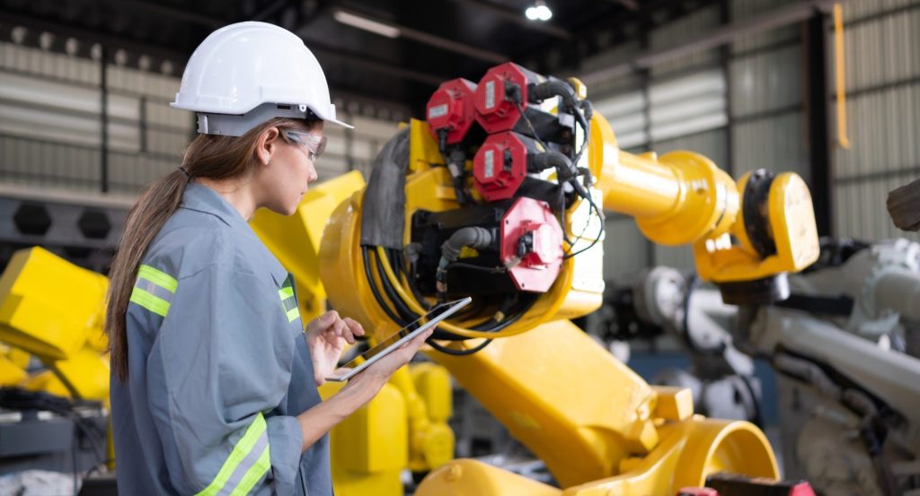 A female engineer installs a program on a robotics arm in a robot warehouse.