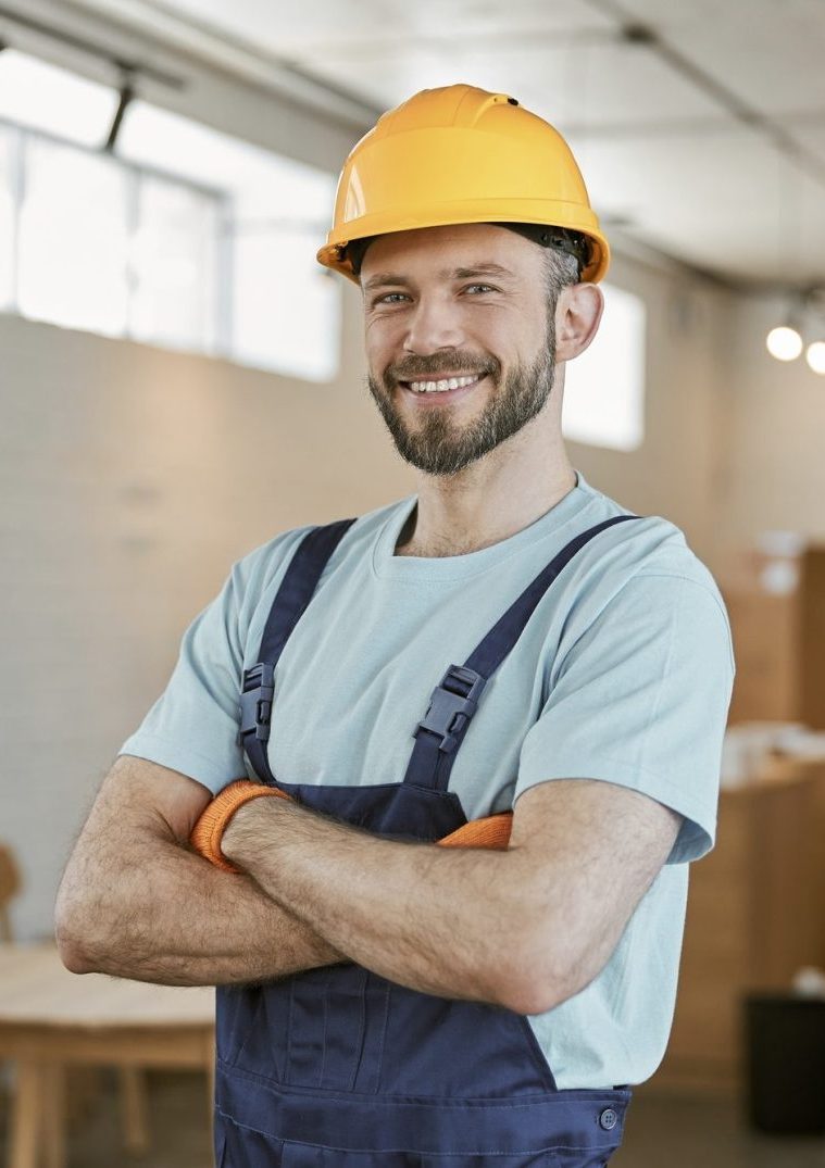 Cheerful male worker in helmet standing in workshop