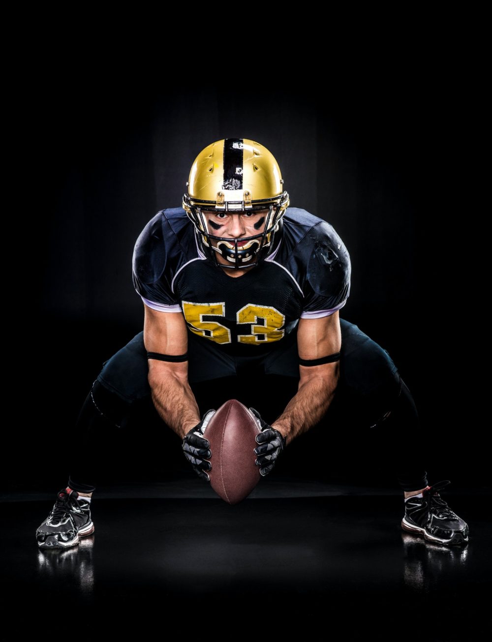 American football player in protective sportswear holding ball on dark
