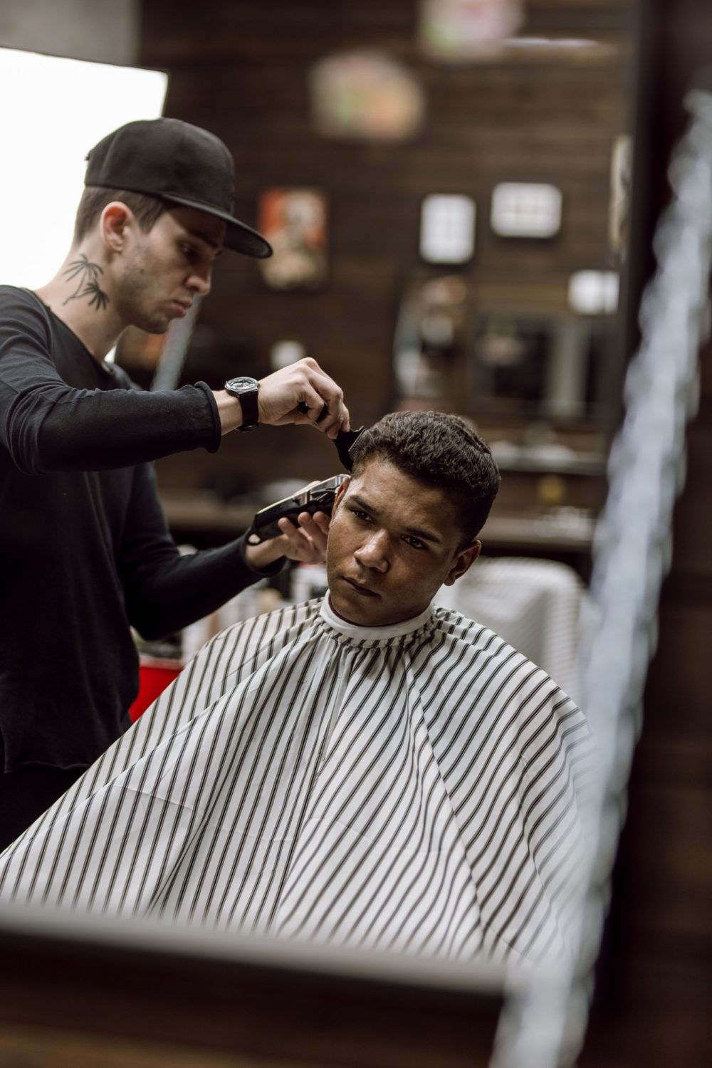 The barber dressed in black clothes makes a razor cut hair back and sides for a stylish man sitting