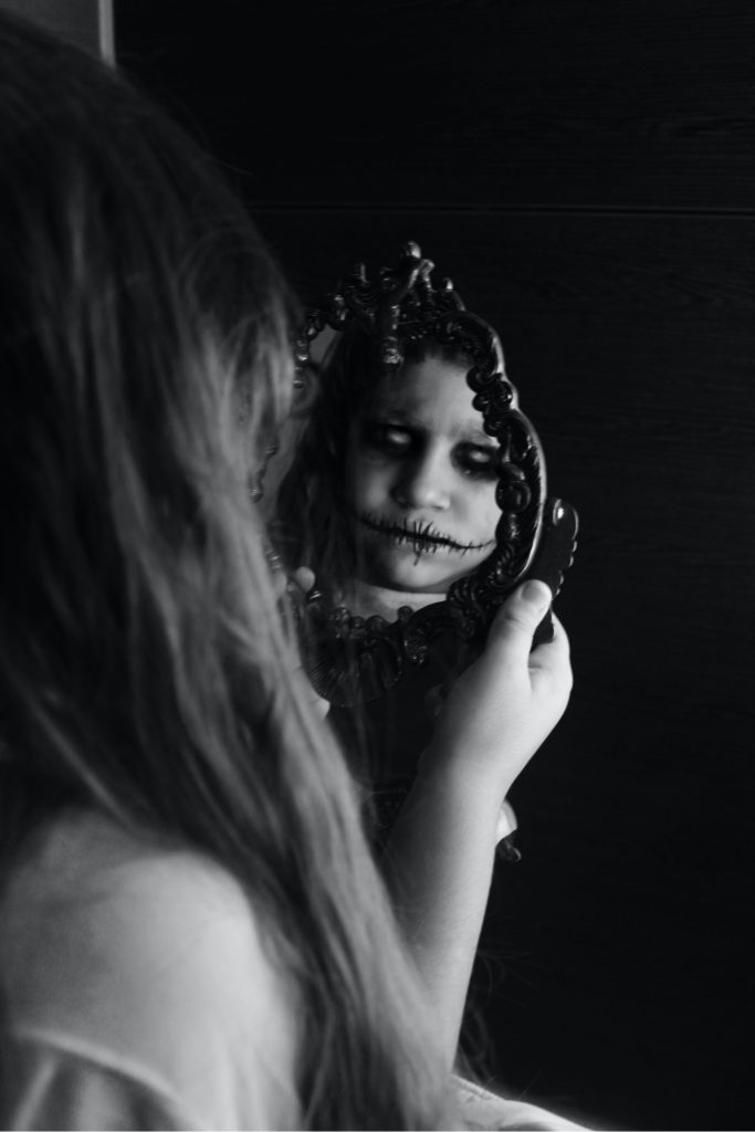 A little girl looking at the mirror to see a spooky reflection