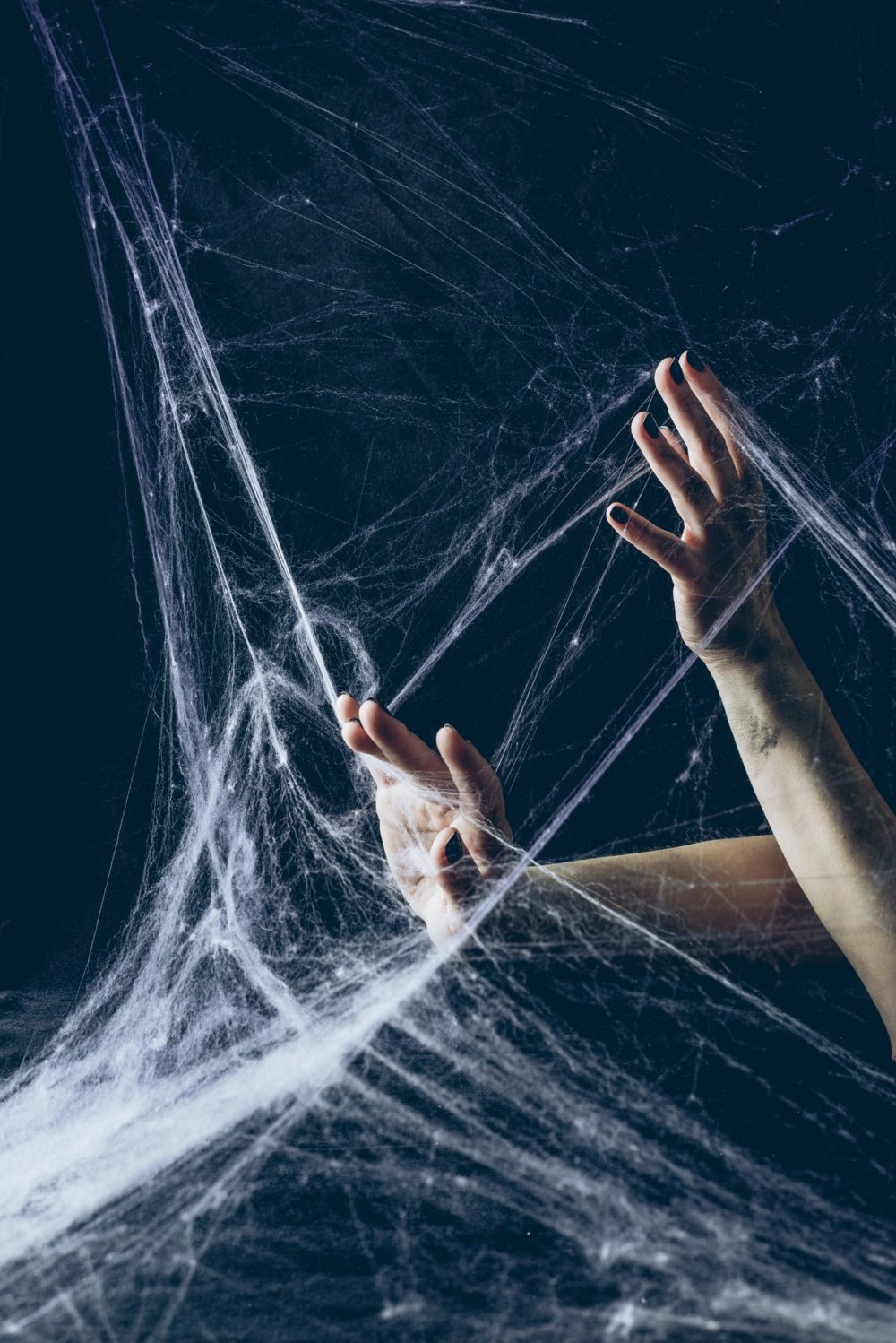 cropped view of gothic woman with hands in spider web in darkness