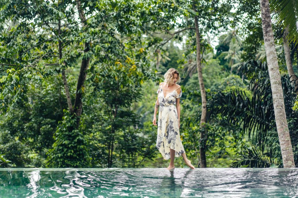 attractive blond woman in dress walking near swimming pool with green plants on background, ubud,