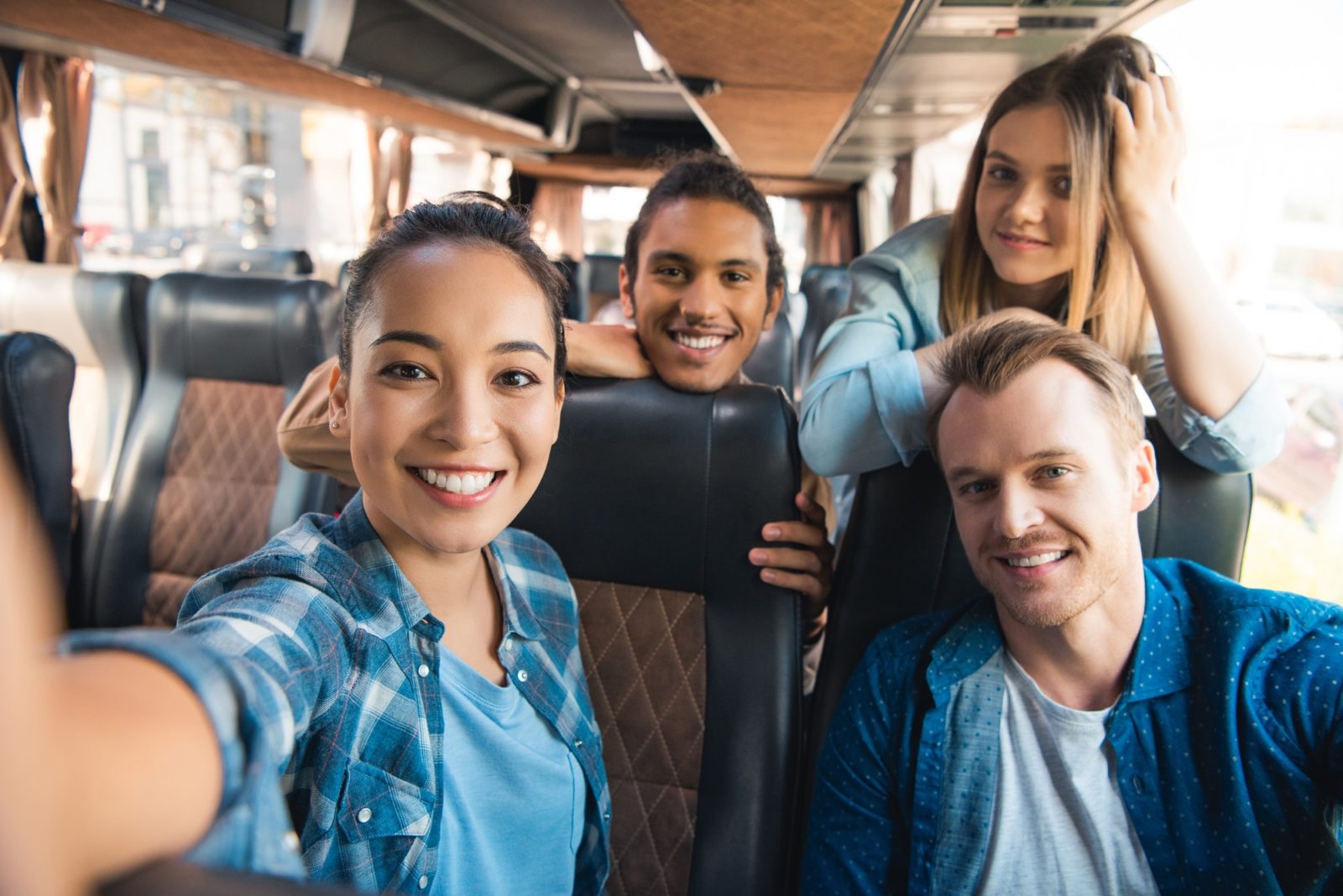 selective focus of smiling asian woman taking selfie with multicultural friends in travel bus