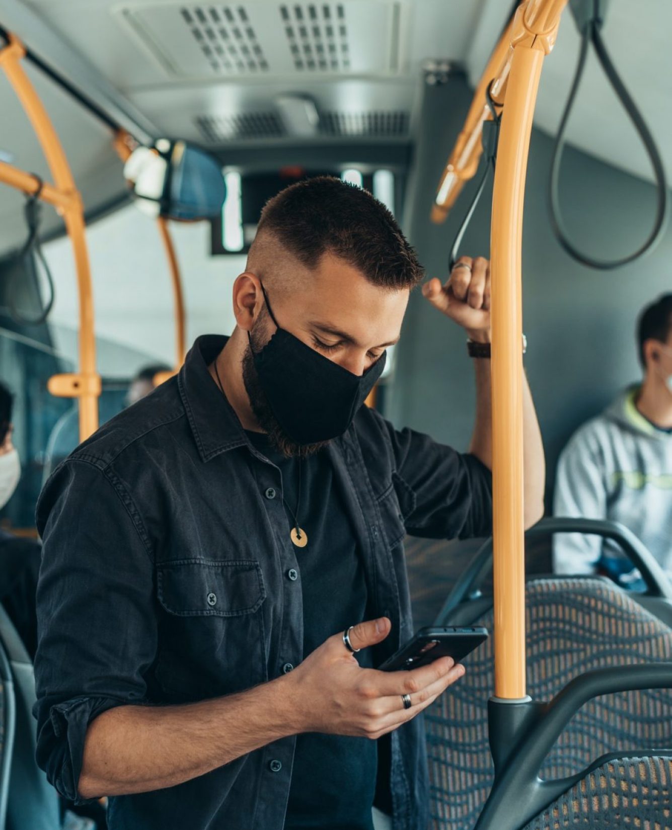 Man wearing a protective mask and using a smartphone while keeping the distance in the bus