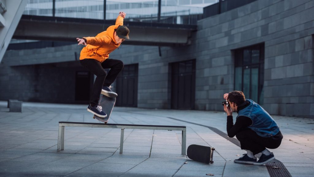man taking photo of skateboarder doing trick over bench