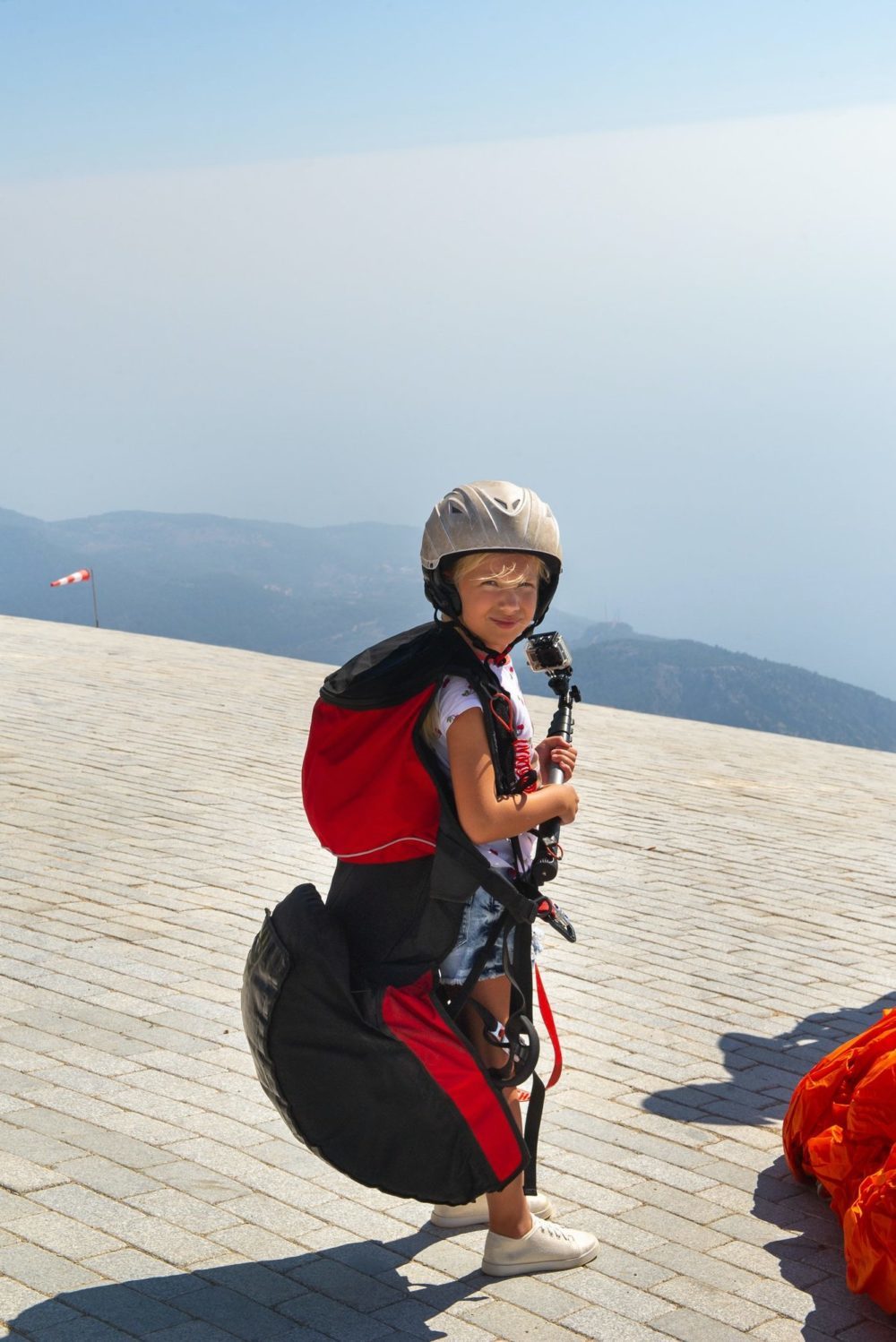 A little girl in paragliding gear and with a camera stands on the edge of Mount Babadag.Turkey
