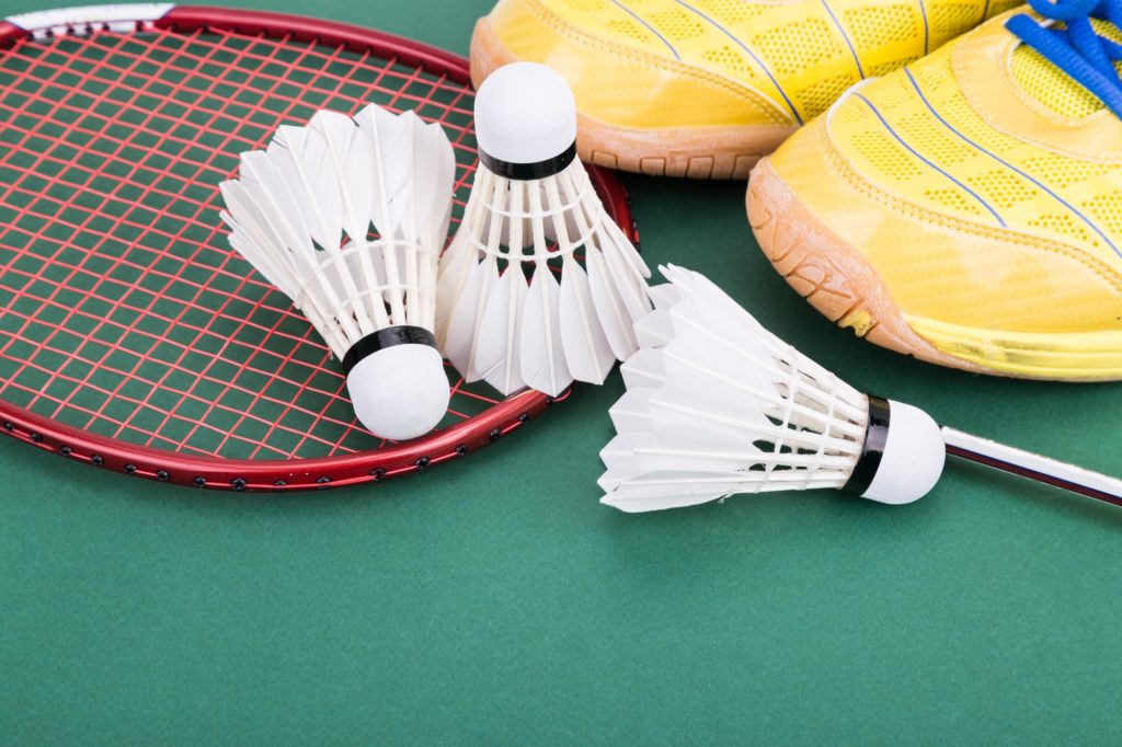 Three badminton shuttlecock with racket and shoes on green court