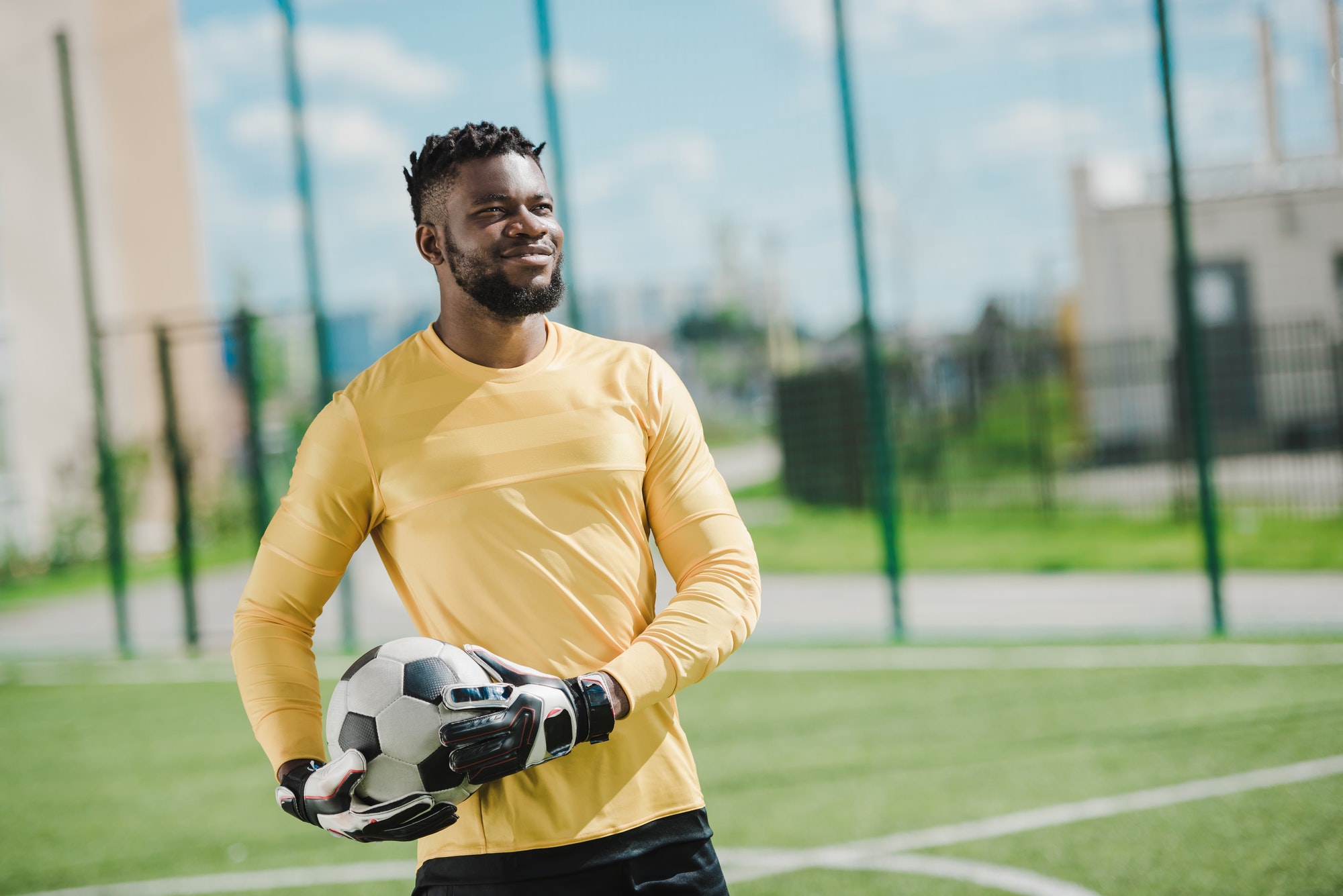 portrait of smiling african american goalkeeper holding ball on soccer pitch