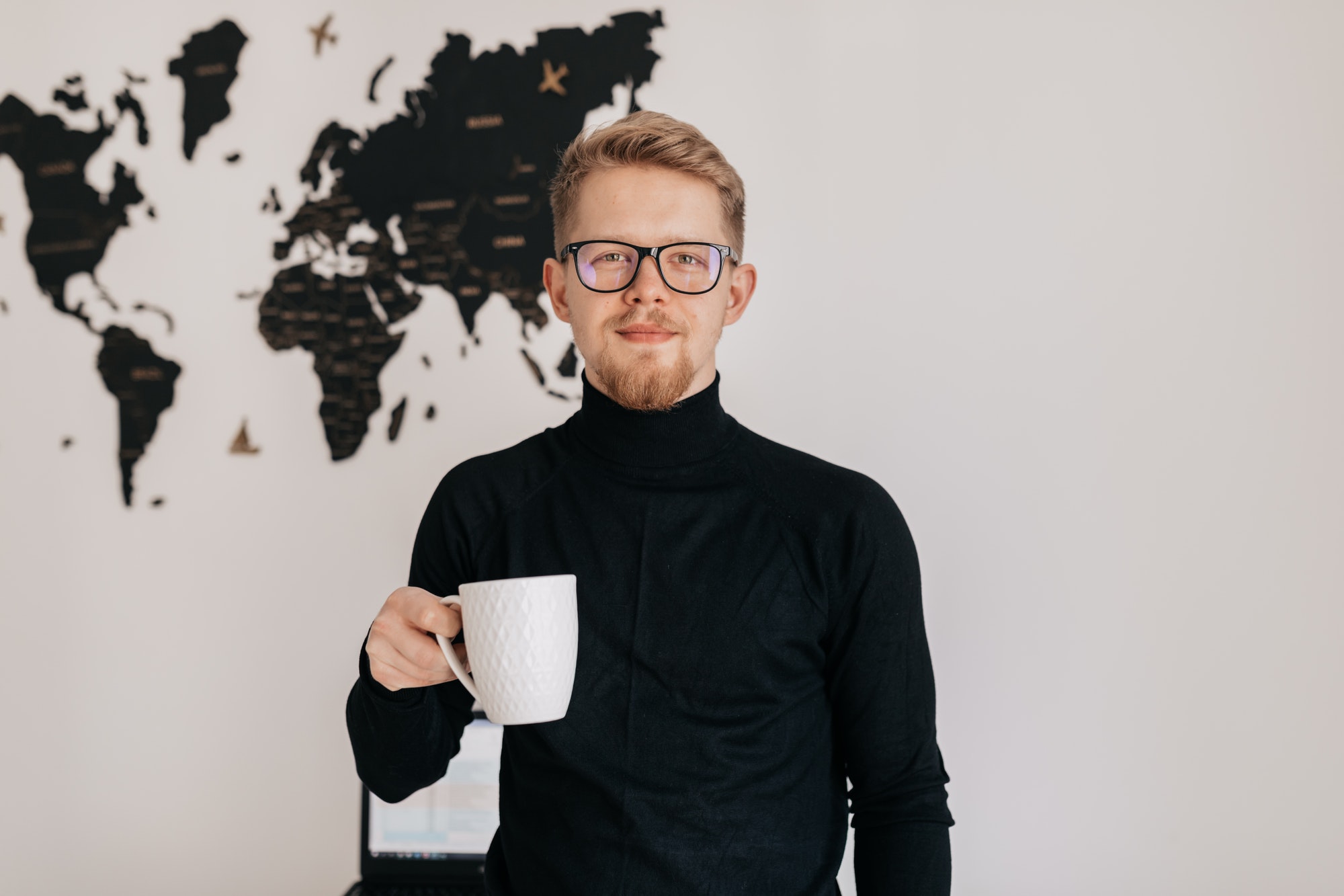 Indoor portrait of handsome blond man in spectaculars and black pullover drinking tea