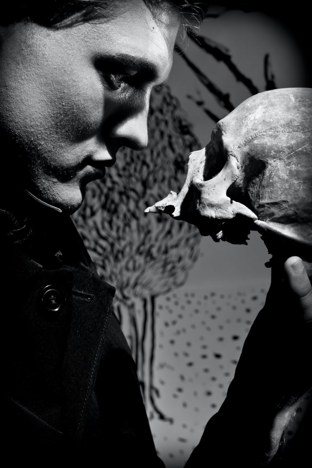 A young man dressed in black with a skull in his hands. Black and white. Artistic background created