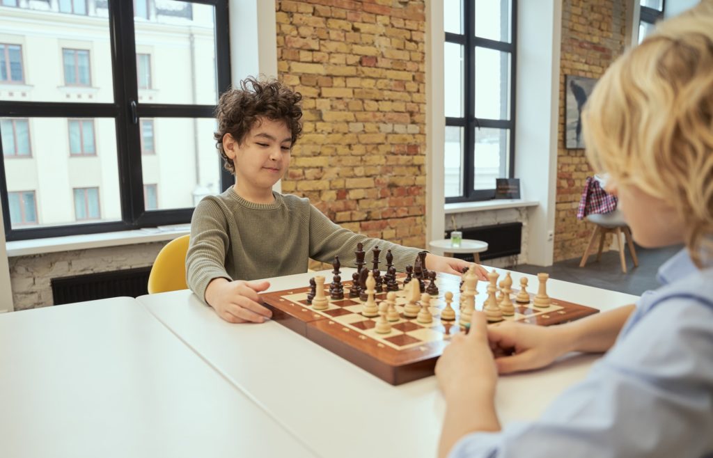 Motivated little boy sitting in the classroom and planning a move while playing chess on the