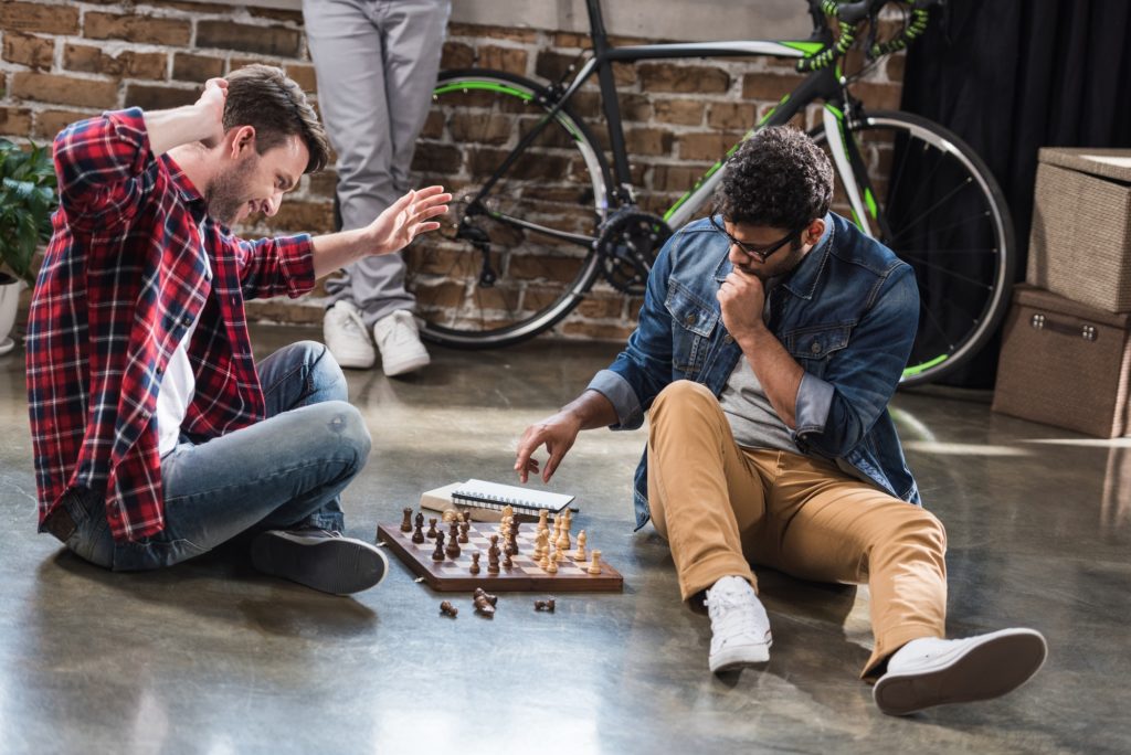 young men sitting on floor and playing chess on chess board