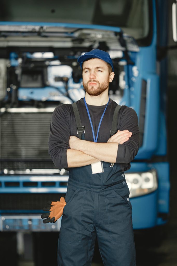 Young worker in uniform near blue truck