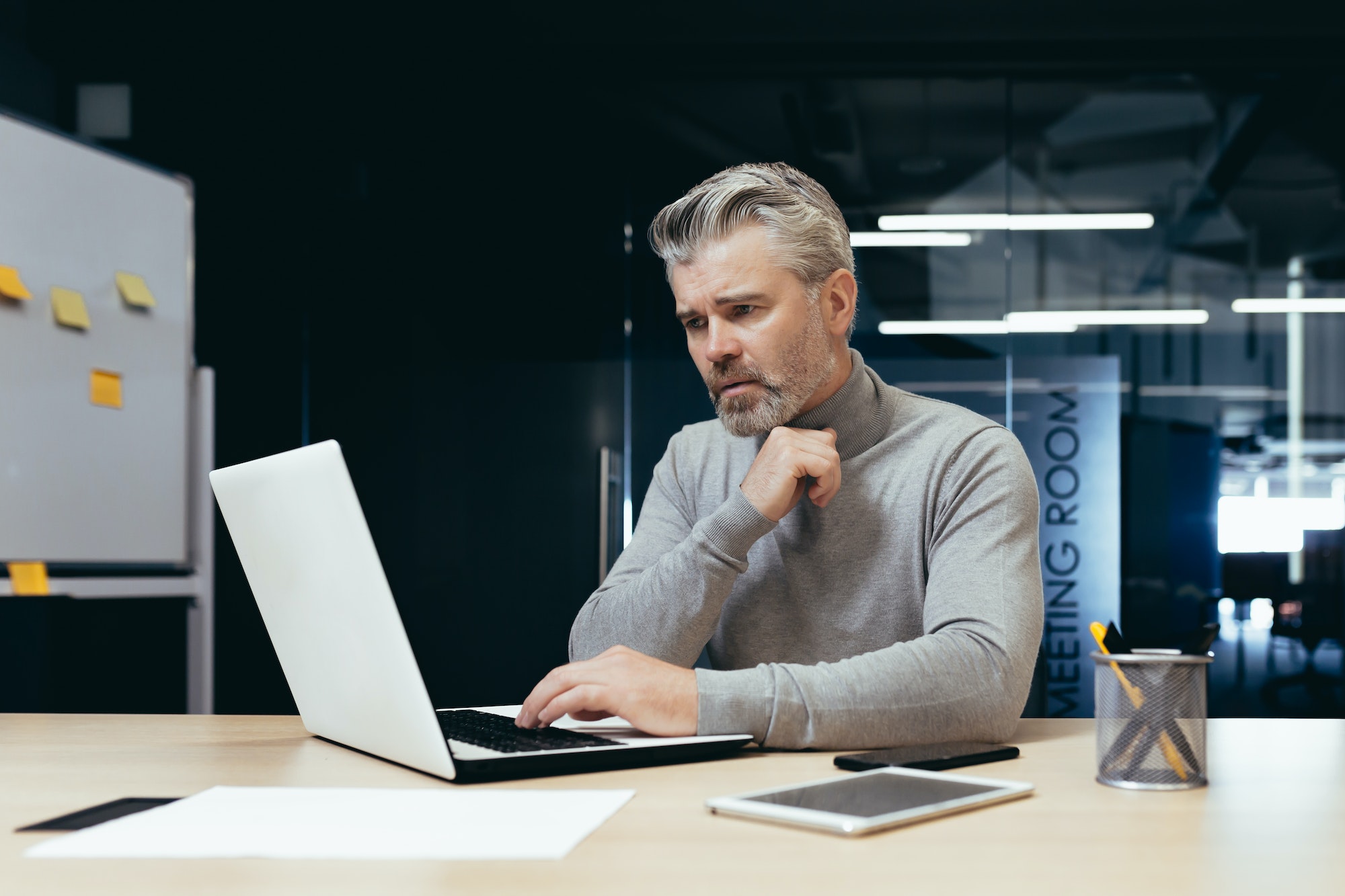 Serious thinking businessman inside office at work with laptop, senior gray haired man working