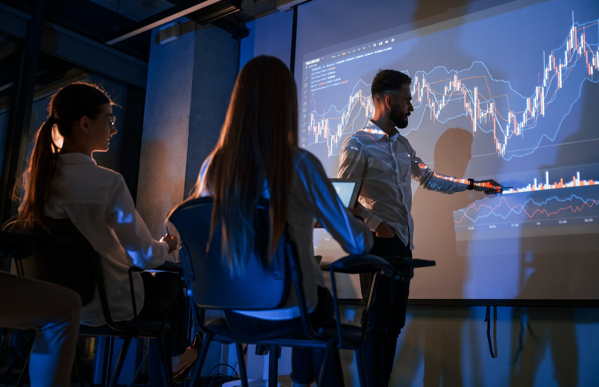 Trading teaching. Male leader talking to employees, showing the plan on the projector in office