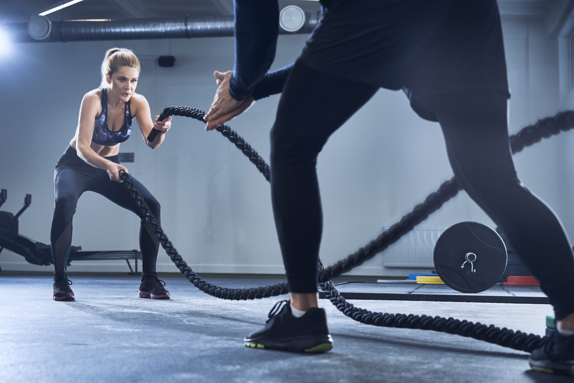 Athletic woman doing battlerope exercise with personal trainer at gym