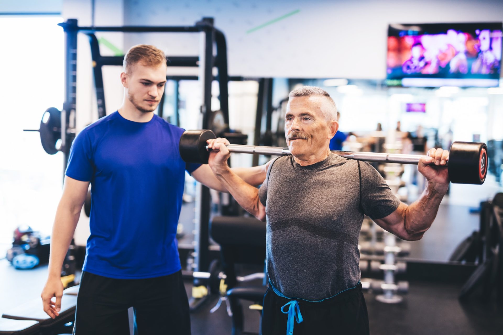 Older man assisting senior man at the gym.
