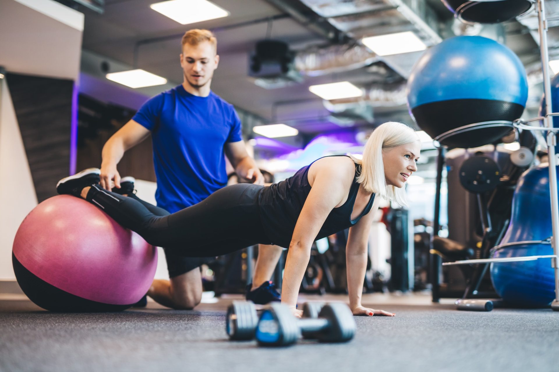 Woman working out on a ball with personal trainer.