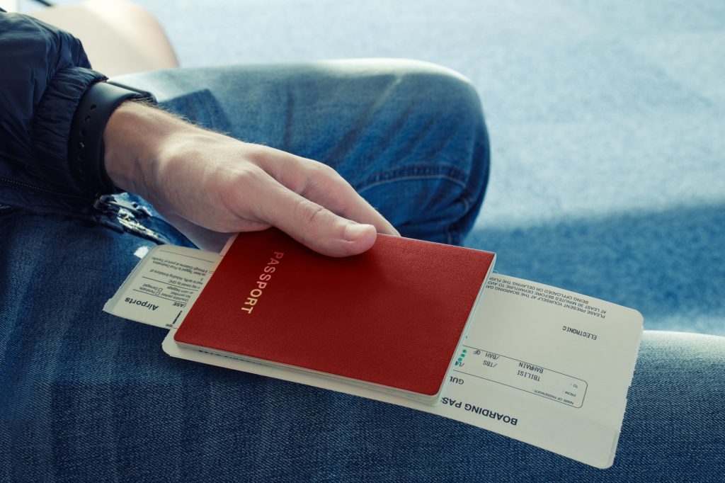 Man in blue jeans sits and holds in his hand passport of red color with tickets to plane