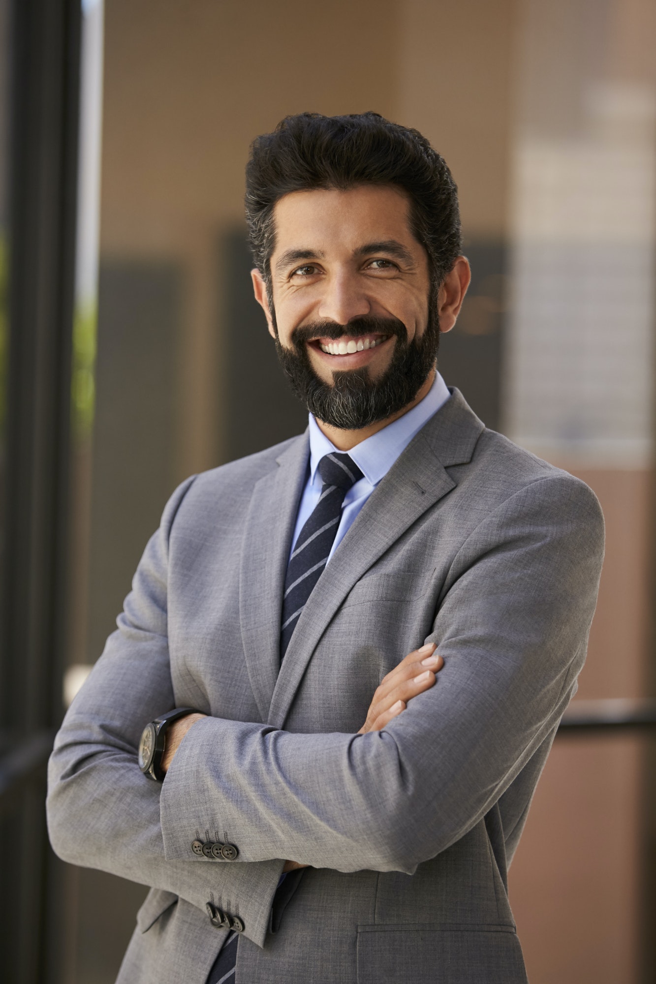 Smiling Hispanic businessman with arms crossed, vertical