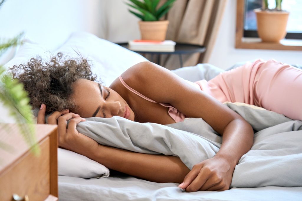 African American young woman sleeping in comfortable bedroom with eyes closed.