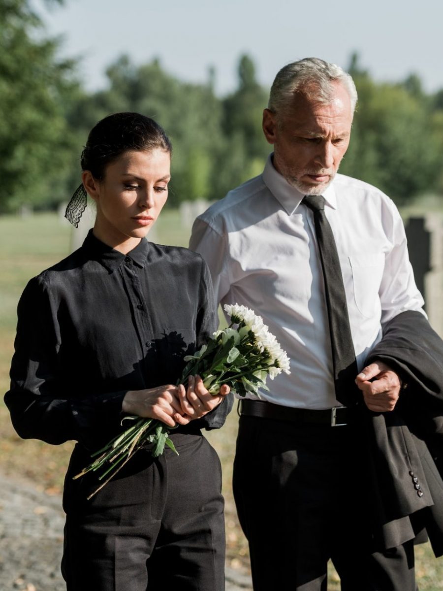 bearded senior man walking near woman with flowers on funeral