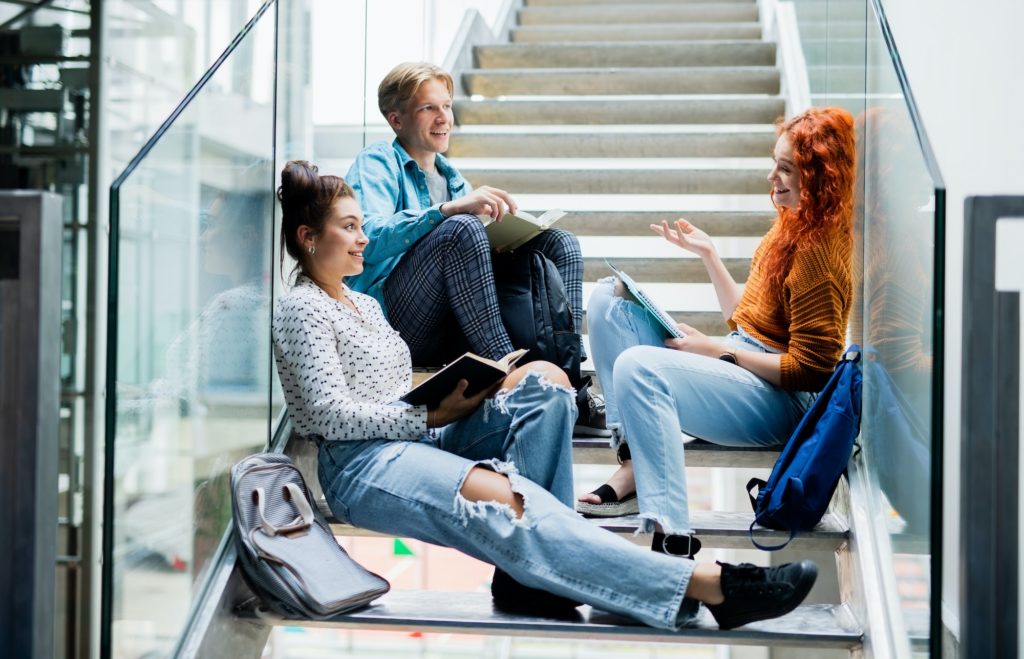 University students sitting on stairs and talking indoors, back to school concept