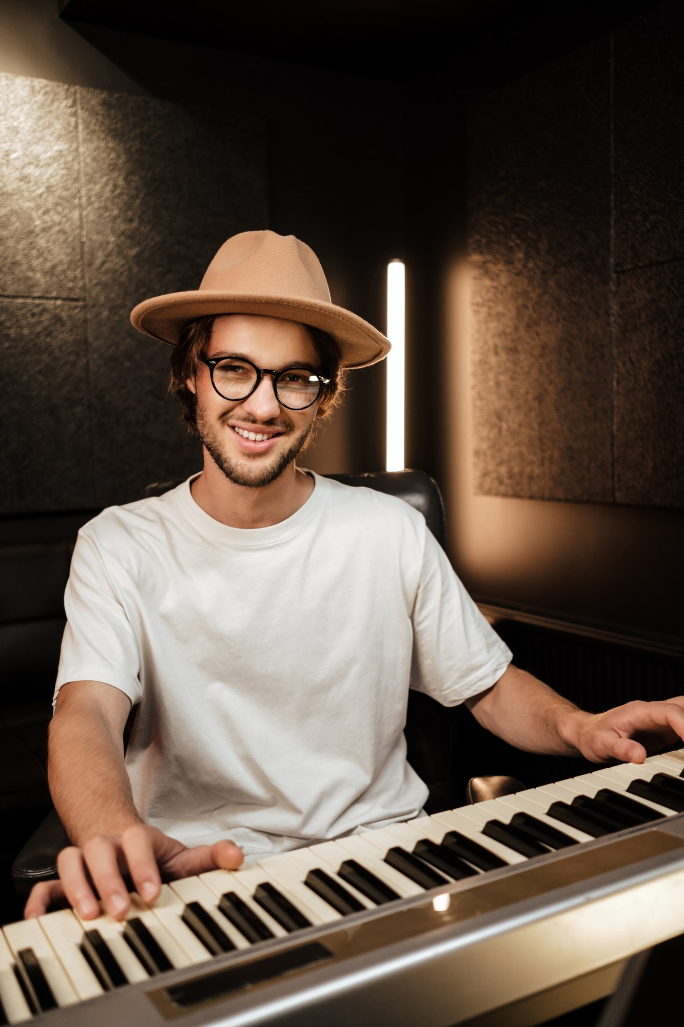 Young stylish music arranger composing song on midi piano in recording studio