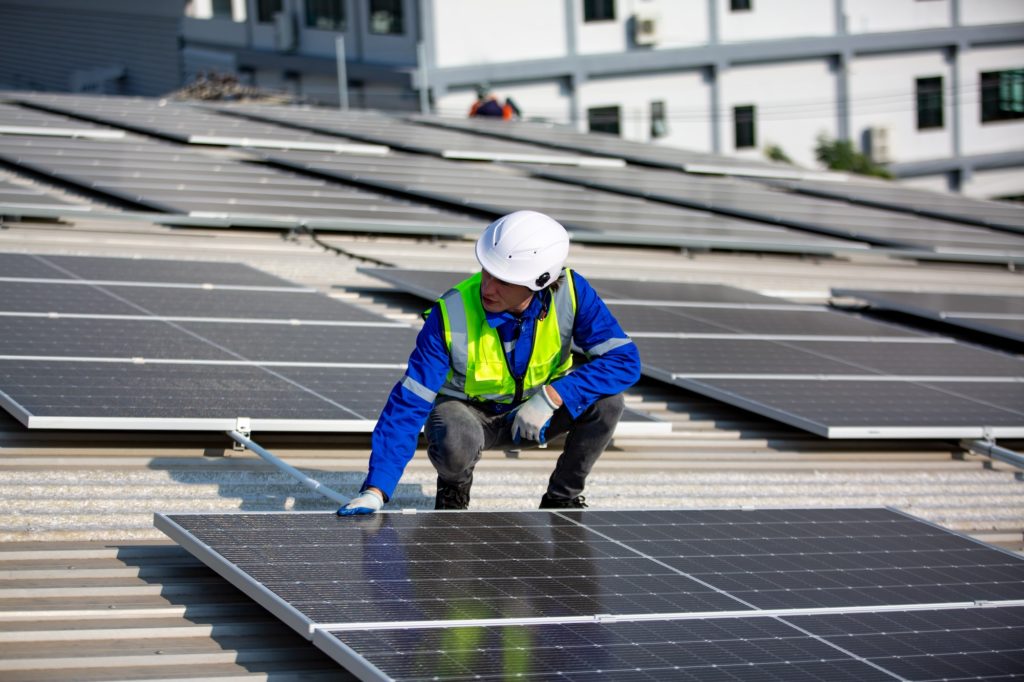 Solar panel installer installing solar panels on roof of warehouse