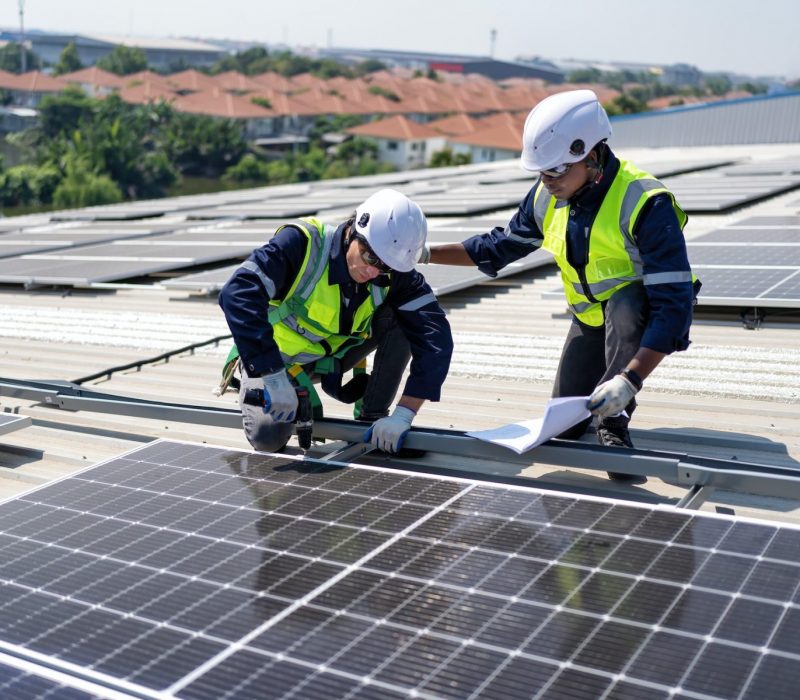 Engineer on rooftop kneeling next to solar panels photo voltaic check drawing for good installation