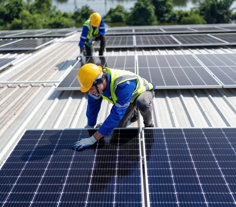 Engineer on rooftop kneeling next to solar panels photo voltaic with tool in hand for installation