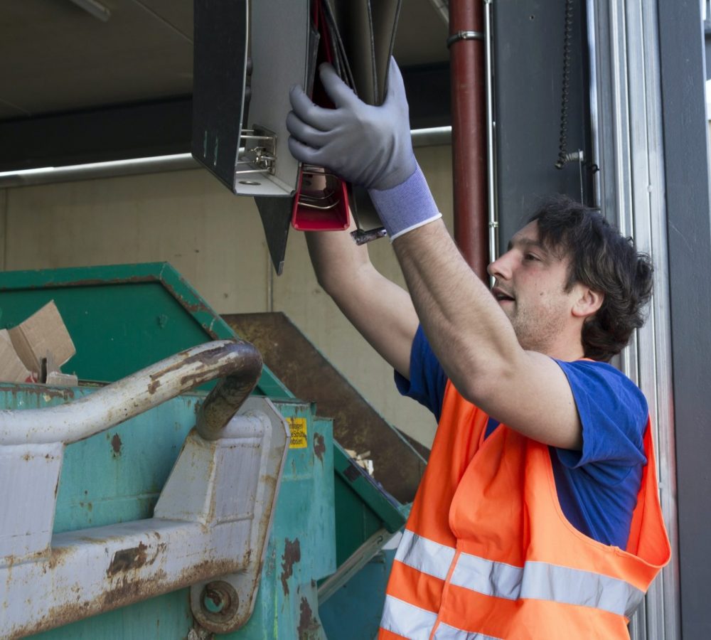 Worker at a waste container throwing away folders