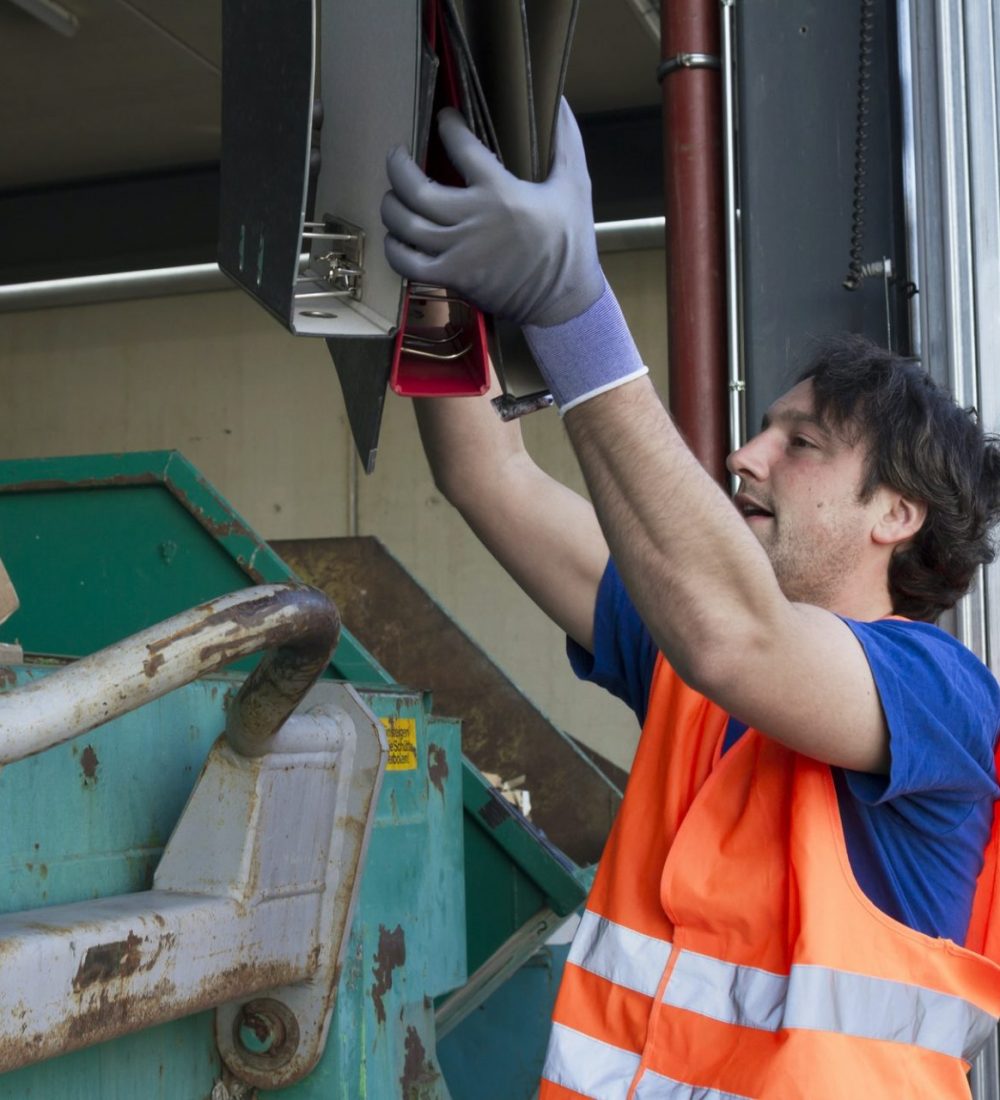 Worker at a waste container throwing away folders