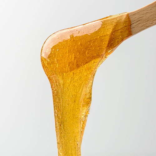 Liquid yellow sugar paste or wax for epilation on wooden stick or spatula closeup