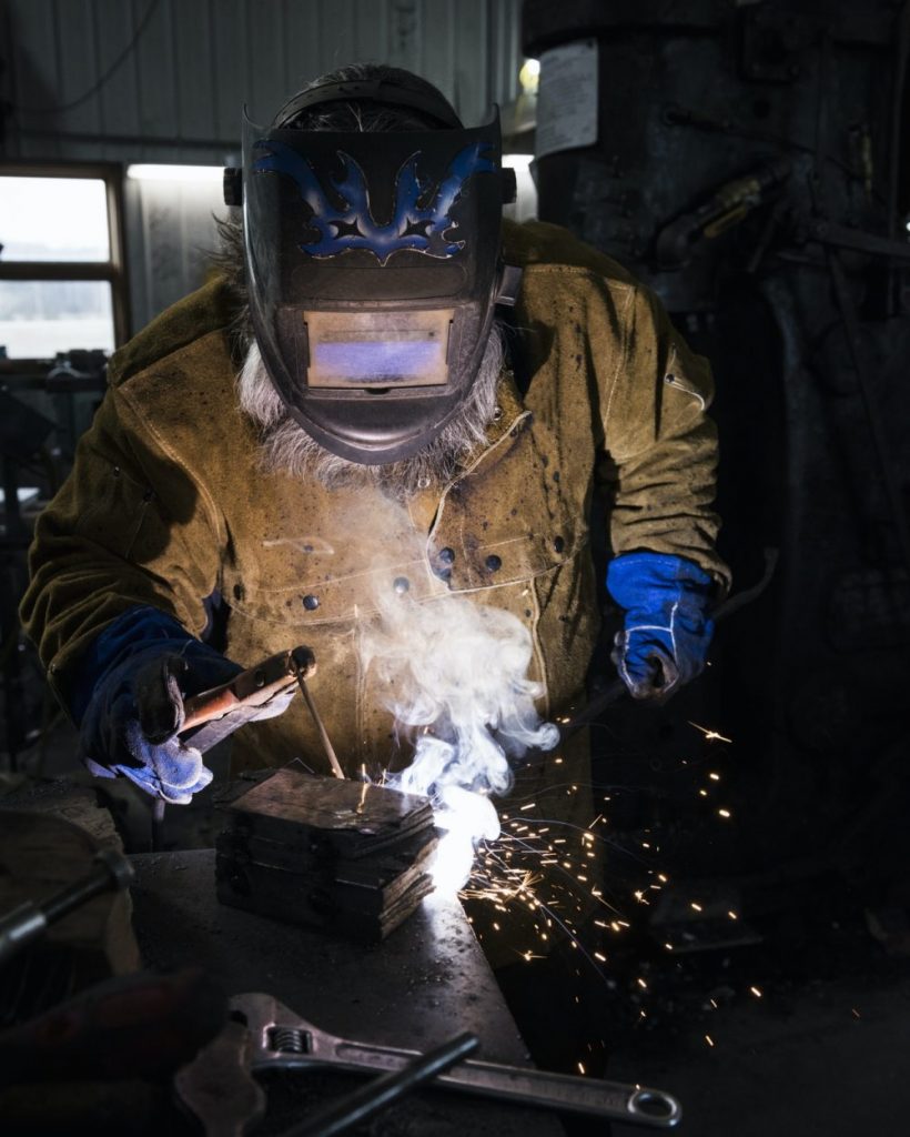 Blacksmith in welding mask welding metal in workshop