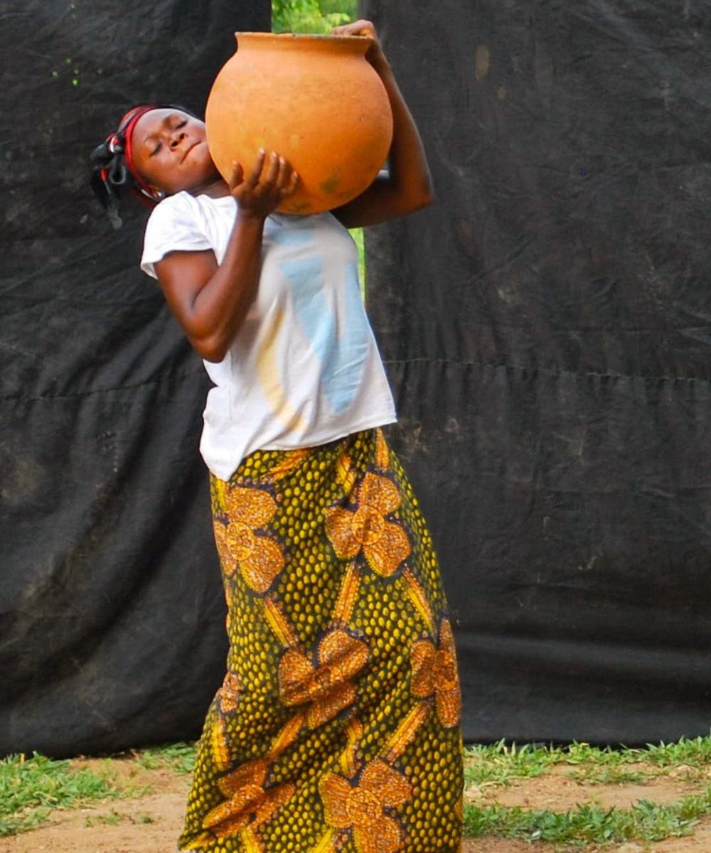 African lady wearing a big jug of water, wearing traditional african clothes