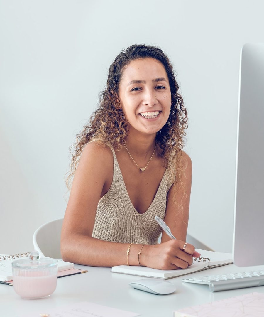 Happy student sitting at table with computer and writing notes in planner
